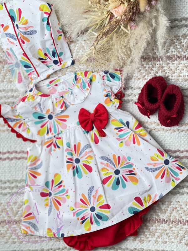 Baby girl white dress with splashes of colors of red teal navy blue yellow orange and pink with a ruffled collar and capped sleeve with a bow on a neutral background.