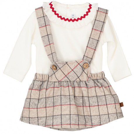 Baby girls cream colored long sleeve top with a ruffled collar with a red zig zag trim paired with a bib style suspender with red, gray , taupe and dark gray checkered print dress on a white background.