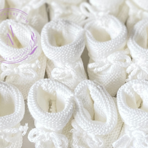 A collage of white knitted newborn baby booties with the cuff turned down and a bow tie.