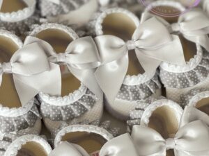 Several grey and white satin baby shoes with a polkadot ruffle trim and bow lined up in rows.