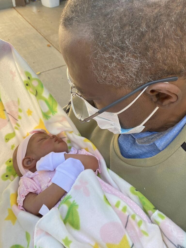 A special grandpa wearing glasses and a mask holding his therapy doll for the very first time.