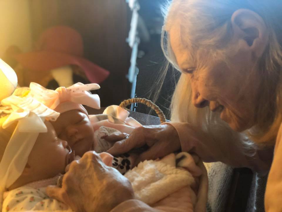 Elderly lady playing with her two reborn therapy dolls in their basket.