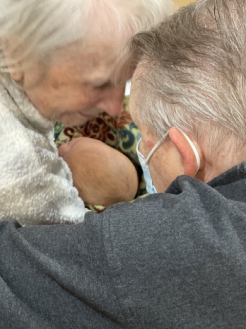 A special brother and sister, grandpa and grandma visiting while sitting down giving kisses to a reborn therapy doll