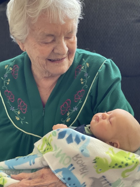 A grandma wearing a green robe holding a reborn baby doll wrapped in a blanket.