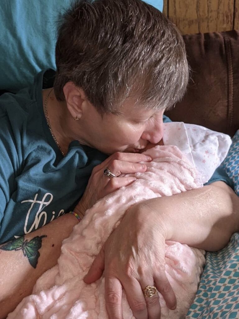 A special Grandma wearing a blue t-shirt sitting in a chair holding her therapy doll for the first time, giving the baby a kiss