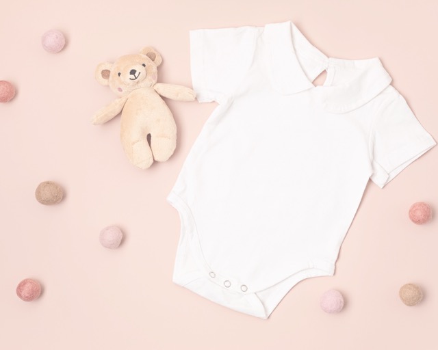 Baby white onesie with teddy bear on a soft pink back drop