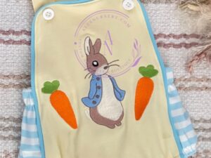 This little baby romper has the softest cream yellow front and straps with an accent printed material with baby blue and white on the sides and back, trimmed in a beautiful blue color with the cutest embroidered bunny and carrots on the bib. Size 6m Sold by Alz's Baby Boutique