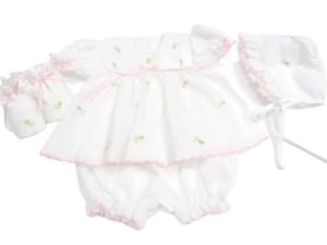This sweet four piece white dress with multi color flowers includes a stunning dress, bloomer, bonnet and baby shoes. All with embroidered pastel color flowers with individual stems. Has a delicate satin ribbon inserted in a white lace white ribbon bow accent. Pink scallop border trim with short puffed and gathered sleeves. Comes in sizes preemie and newborn. Made in Columbia Sold by Alz's Baby Boutique