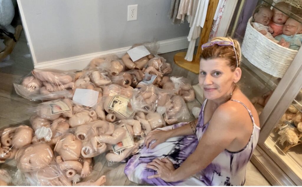 Ginger Kelly with Alz's Nursery surrounded by numerous doll kits donated to the nursery to give away.