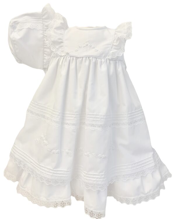 Delicate heirloom dress has layers of delicate lace trim, with beautiful embroidered flowers and tiny pearl accent. Has rows of pleated details around the entire dress. Buttons and ties at the back with sash bow. Made in Columbia Poly cotton blend Sold by Alz's Baby Boutique